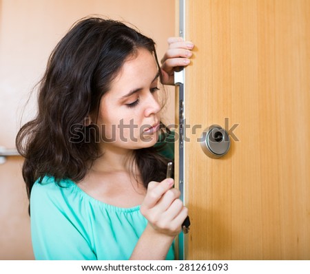 Sad young long-haired woman looking at broken lock of outer door