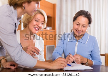 Two smiling senior ladies signing documents at bank with agent