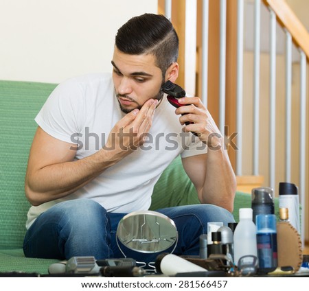 young european man looking at mirror and shaving beard with trimmer
