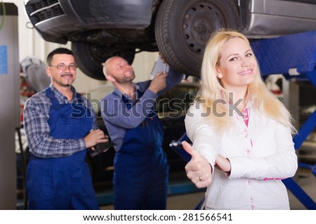 Service crew and happy driver standing near car and smiling indoor. Focus on woman