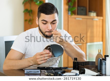 Adult russian man plucking hair from his nose with pliers