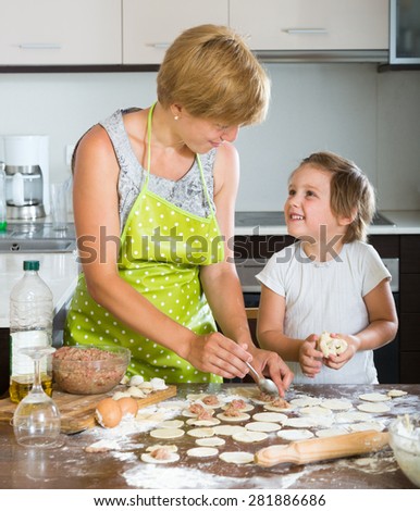Happy child with woman making traditional meat dumplings from meat stuffing and dough