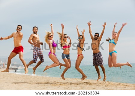 Positive adults jumping at sandy beach in summer day