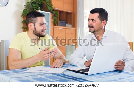 Positive insurance agent with laptop giving presentation to a male client at home