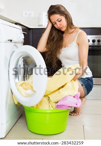 Home laundry. Tired young housewife with clothes near washing machine at home