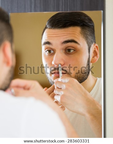 Young male in front of mirror remove hair from his nose with scissors