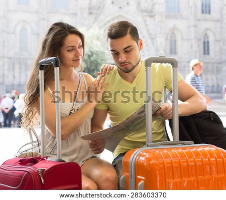 Young travelers with suitcases sitting and looking at a map of the city