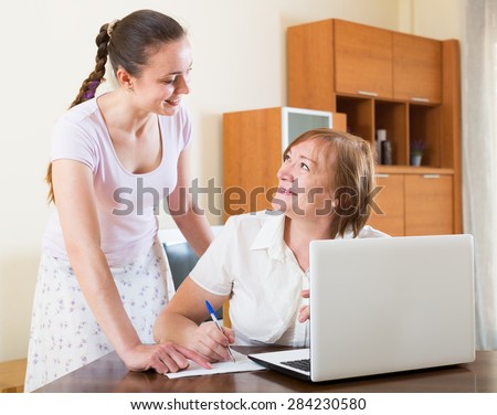smiling russian women with financial documents and laptop at table in home interior