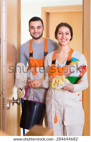 Portrait of professional cleaners with equipment standing at doors of client house