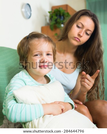 Young mother scolding crying child at home. Focus on girl