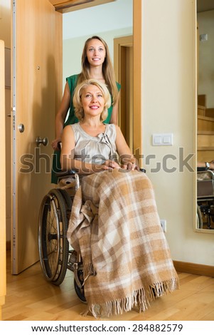Girl helping handicapped elderly woman to enter the apartment. Focus on mature