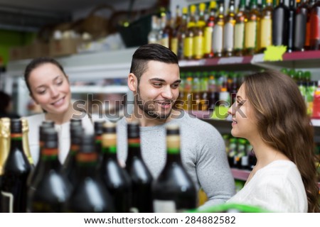 Adult positive shoppers choosing bottle of wine at liquor store