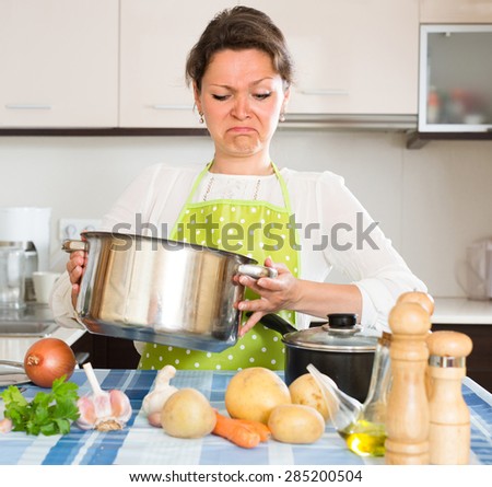 Upset housewife in apron feeling bad smell from pan at domestic kitchen