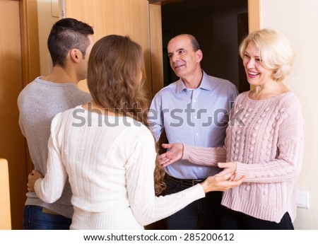 Happy young couple inviting elderly parents to come inside