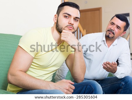 Two male adults sitting on couch and being at odds at home