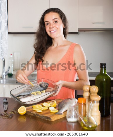 Happy woman cooking fish  in frying pan at home kitchen