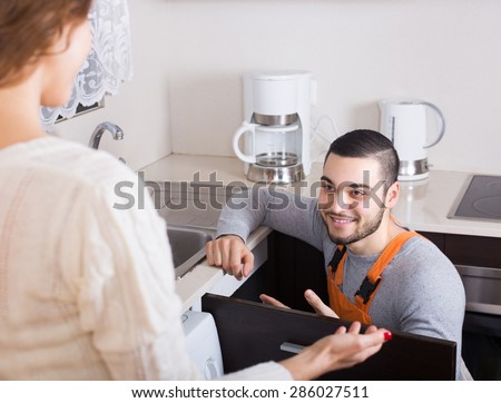 Woman watching professional worker repairing water lines at home kitchen