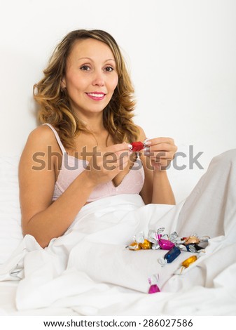 Adult smiling woman eating candy in bed at home