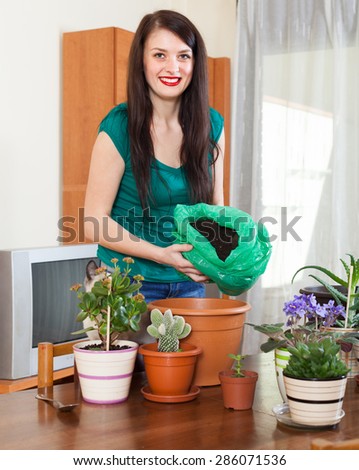 Smiling girl working with  flowers in pots at table in home