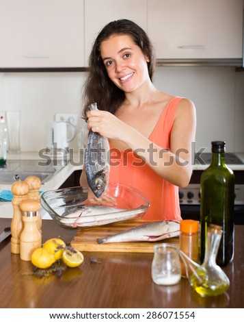 Smiling brunette woman cooking fish in home kitchen