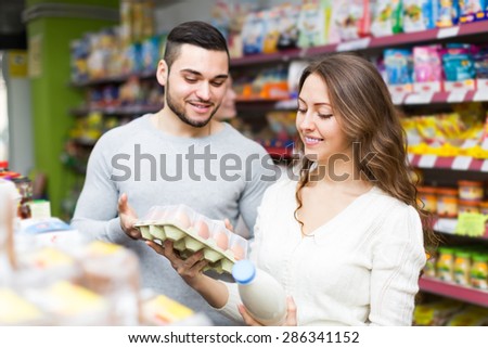 Positive customers choosing milk and eggs at store and smiling. Focus on girl