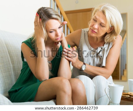 Mature mother comforting crying daughter at home. Focus on young