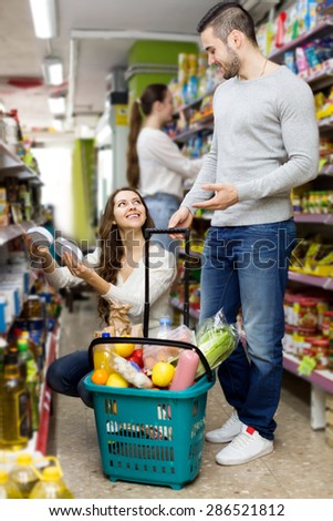 Young happy couple standing near shelves with canned goods at shop. Focus on the woman