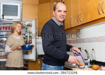Elderly smiling husband helping wife to cook indoors