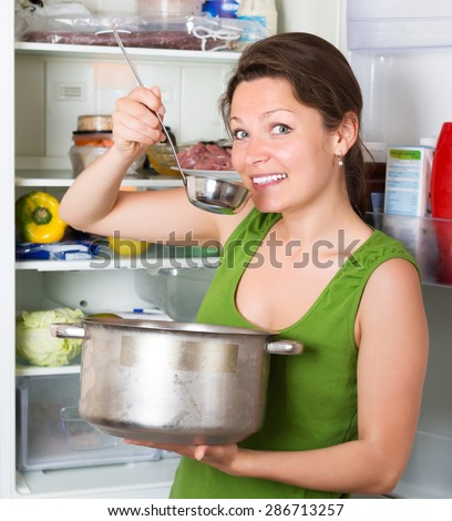 Hungry happy woman eating  soup from pan near fridge  at kitchen