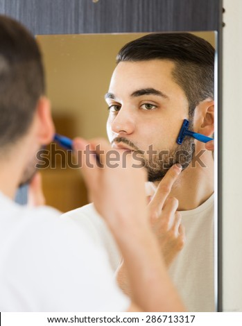 russian man looking at mirror and shaving face with razor