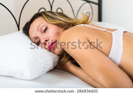 Middle-aged blonde long-haired woman sleeping in bed at home
