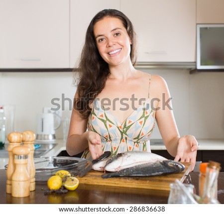 Smiling young brunette woman with fish at home kitchen