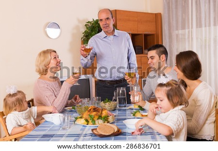 Smiling housefather says toast at the dinner table in front of his friendly family indoor
