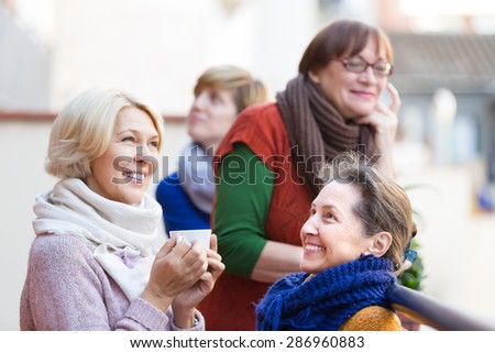 Happy smiling elderly females drinking coffee at patio. Focus on brunette