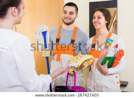 Smiling housewife meeting cleaning crew with equipment at apartment doorway. Focus on man
