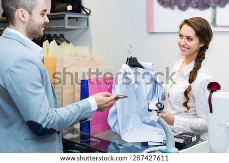 Positive male client paying by card for new clothes at store counter