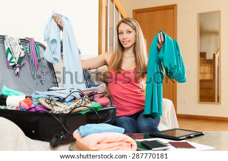 Smiling attractive girl sitting near scattered clothes and packing luggage