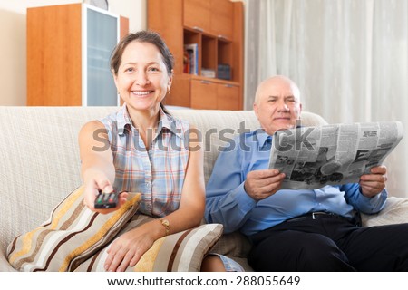 Happy couple grandparents reading a newspaper at home