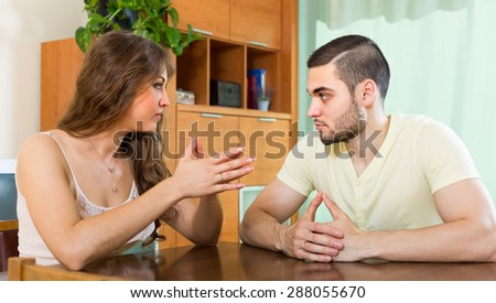 Serious young couple talking at the table in home interior
