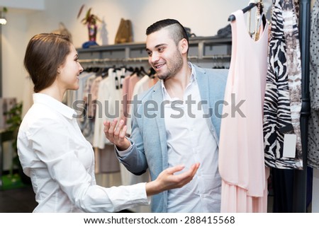 female assistant helping young man to choose new garment at boutique. Focus on the man