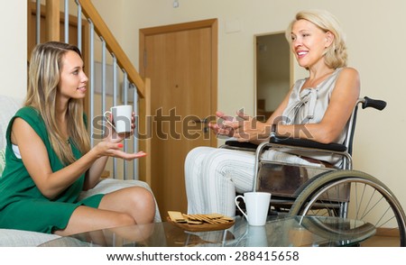 Happy women in wheelchair and girl drinking tea at home. Focus on young