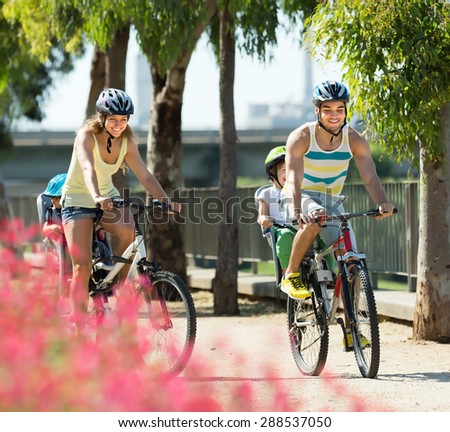 Happy active family of four cycling on street road in summer day
