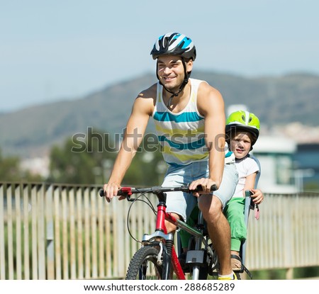 Happy father with daughter in helmets cycling though street