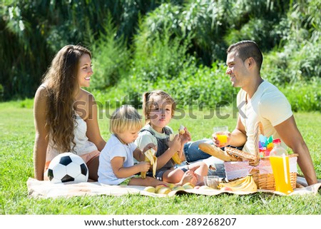 Young smiling couple with little daughters having holiday with picnic