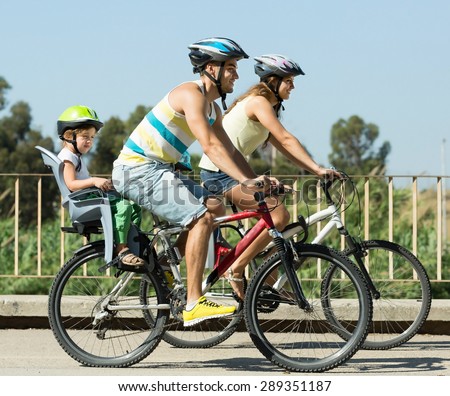 Active young happy parents with two kids cycling on street road