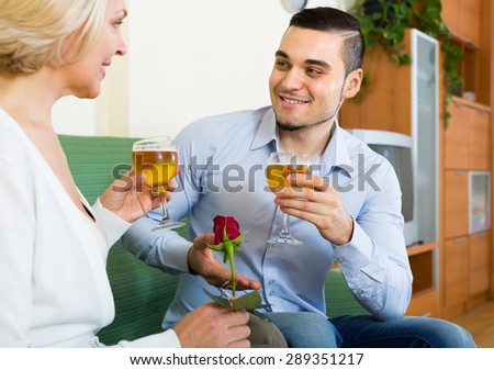 Happy senior woman with smiling young boyfriend drinking wine at home