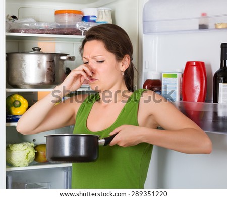 Girl holding her nose because of bad smell from food near refrigerator  at home