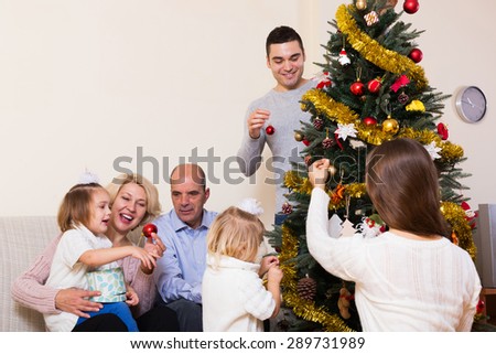 Happy adults and little kids helping grand parent decorate Xmas tree at home