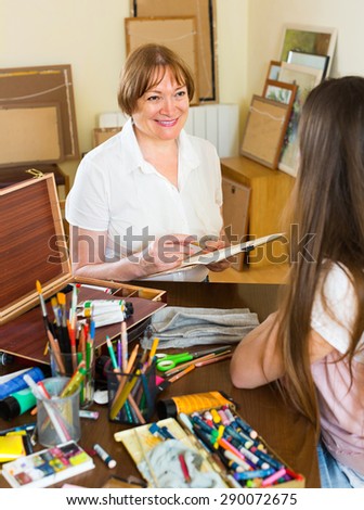 Smiling mature female artist painting portrait of longhaired girl at art studio