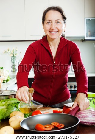Happy mature woman pouring oil into girdle at kitchen